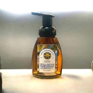 May include: A clear, amber-colored foaming hand soap bottle with a black pump. The label reads "Sunflower Beach Co. Seaside Resort" with a sunflower graphic. The bottle contains 8 fl oz (236ml) of soap.