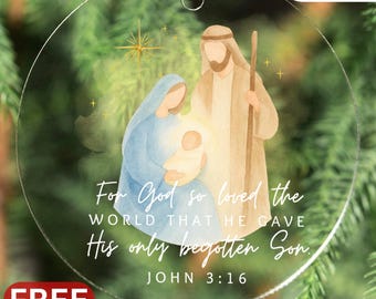Puede incluir: Adorno navideño redondo y transparente con una ilustración en acuarela de la escena de la Natividad. El adorno presenta a María, José y el niño Jesús, con el texto "For God so loved the world that He gave His only begotten Son. John 3:16."