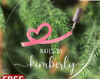 May include: Clear, round ornament with a pink heart design and the text "NAILS BY kimberly". A nail polish brush is applying pink polish. Includes a white ribbon for hanging. The word "SALE" is in a red box.