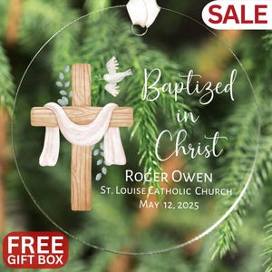 Op de afbeelding: Transparante, ronde ornament met een kruis, duif en de tekst "Baptized in Christ". Bevat de naam Roger Owen, kerkgegevens en datum. Een wit lint is bevestigd om op te hangen. Het woord "SALE" staat rechtsboven en "FREE GIFT BOX" linksonder.