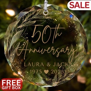 May include: A clear, faceted glass ornament with the words "50th Anniversary" in gold script. The names "Laura & Jack" and the years "1975 2025" are also inscribed. The ornament has a silver string for hanging and is decorated with gold leaf accents.