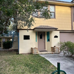 Può includere: Un edificio giallo con una porta marrone e un vialetto di mattoni. L'edificio ha un tetto marrone e un prato verde di fronte.