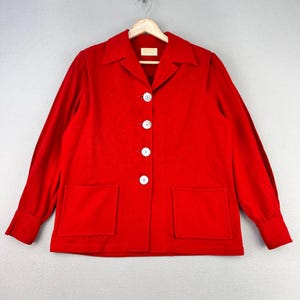 May include: A bright red jacket with a collared neckline, long sleeves, and two front pockets. The jacket features four white buttons down the front and is hanging on a wooden hanger.