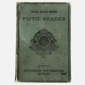 May include: A vintage Fifth Reader book with a green cover. The cover features the text "DE LA SALLE SERIES" at the top, with "FIFTH READER" below. A crest with a star and the words "SIGNUM" and "FIDEL" is in the center. The bottom reads "BROTHERS OF THE CHRISTIAN SCHOOLS."