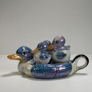 May include: A set of three ceramic mugs with a speckled, matte finish. The mugs are in shades of cream, light gray, and dark gray. Each mug has a simple, minimalist design and a rounded handle.