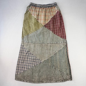 May include: A patchwork skirt featuring a variety of plaid and patterned fabrics in shades of green, red, blue, and brown. The skirt has an elastic waistband and a long, flowing silhouette, suitable for casual wear.