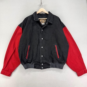 May include: Black and red denim jacket with a button-up front and a collar. The jacket has red sleeves and two front pockets with red trim. The jacket is hanging on a wooden hanger.