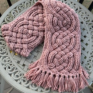 May include: A pink crocheted scarf with a Celtic knot pattern and fringe tassels.