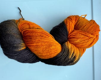May include: A skein of yarn with orange and black color variations. The yarn is made of wool and is suitable for knitting or crocheting.