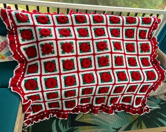 May include: A crocheted throw blanket with a red and white checkered pattern and red rose motifs. The blanket has a white crocheted border with a scalloped edge.
