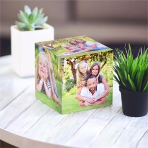 Op de afbeelding: Een houten fotokubus met zes zijden, elk met een andere foto van een gezin in een park. De foto's tonen een man, een vrouw en twee kinderen.