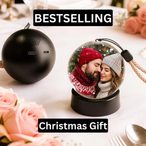 Può includere: Un altoparlante sferico nero e una palla di neve con la foto di una coppia sono esposti. La palla di neve poggia su una base nera e ha un cordino nero. I testi "BESTSELLING" e "Christmas Gift" sono visualizzati.