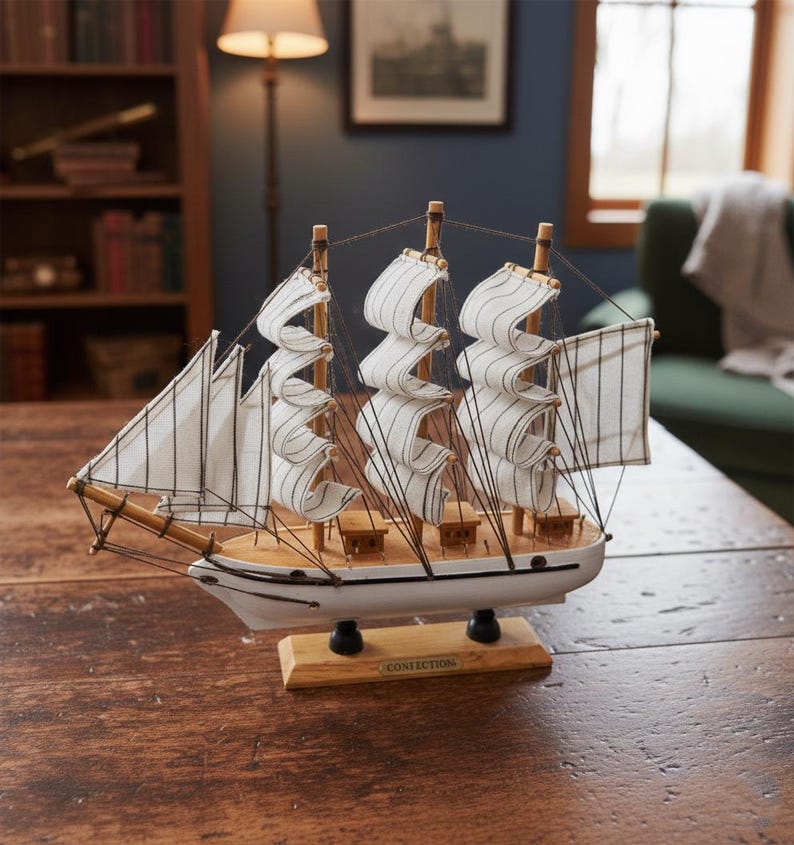 May include: A detailed model sailboat with white sails and a wooden hull. The sails are striped, and the boat is mounted on a wooden base. The model is displayed on a dark wooden table, showcasing nautical decor.