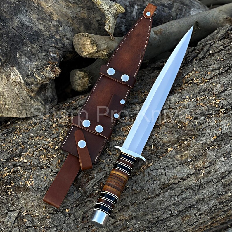 May include: A dagger with a polished steel blade and a handle wrapped in brown and black leather. The dagger is displayed next to its brown leather sheath, which has silver rivets and a belt loop. The dagger and sheath are on a wooden surface.