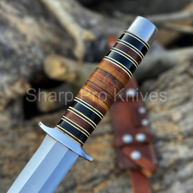 May include: Close-up of a hunting knife with a polished steel blade and a handle featuring alternating layers of black, brown, and cream-colored materials. The text "Sharp Pro Knives" is visible. A leather sheath is in the background.