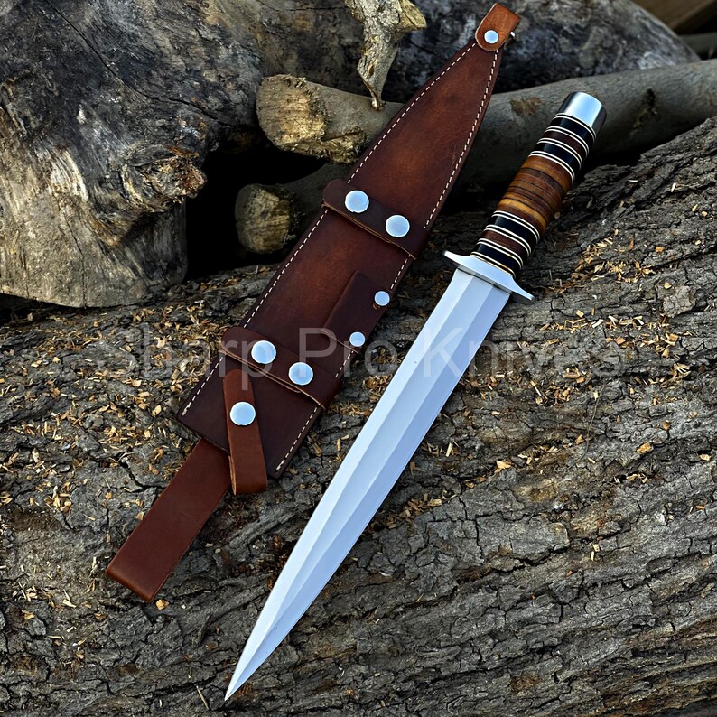 May include: A dagger with a silver blade and a brown and black handle, resting on a wooden surface. The dagger is accompanied by a brown leather sheath with silver rivets. The text "Sharp Pro Knives" is partially visible.