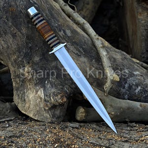 May include: A dagger with a polished silver blade and a handle featuring alternating bands of brown leather and black and silver metal. The text "Sharp Pro Knives" is visible on the wood background.