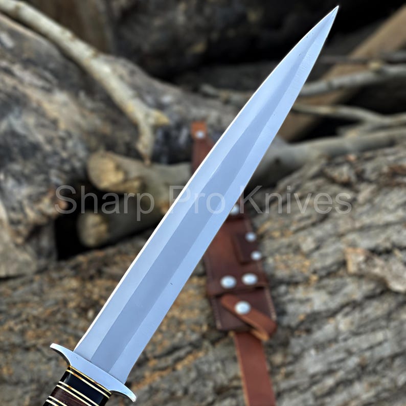 May include: A silver-colored dagger with a sharp point and a brown leather sheath. The handle is wrapped with dark brown and gold bands. The text "Sharp Pro Knives" is visible on the blade.