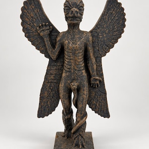 May include: A dark brown, textured statue of the Mesopotamian demon Pazuzu, featuring large wings, a canine-like head, a scorpion tail, and a snake-like phallus. The figure stands on a rectangular base with one arm raised and one arm lowered.