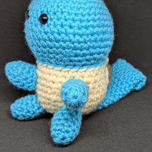 May include: A crocheted blue and cream-colored stuffed toy resembling a turtle with black eyes.