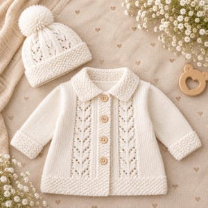 Peut inclure: Un gilet en tricot couleur crème avec un col, des manches longues et quatre boutons en bois sur le devant, présentant un motif de dentelle vertical en forme de feuille. Accompagné d'un bonnet en tricot assorti avec un gros pompon.
