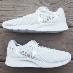 Puede incluir: Un par de zapatillas deportivas blancas con una parte superior de malla y suela blanca. El logotipo de Nike, el swoosh, est&aacute; adornado con brillantes pedrer&iacute;a. Zapatillas dise&ntilde;adas para la comodidad y el estilo.