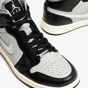 Op de afbeelding: Paar hoge sneakers in zwart, grijs en wit. De sneakers hebben zwarte veters, een grijze neus en een witte zool. Het Air Jordan-logo is zichtbaar op de tong. Geschikt voor sport en dagelijks gebruik.