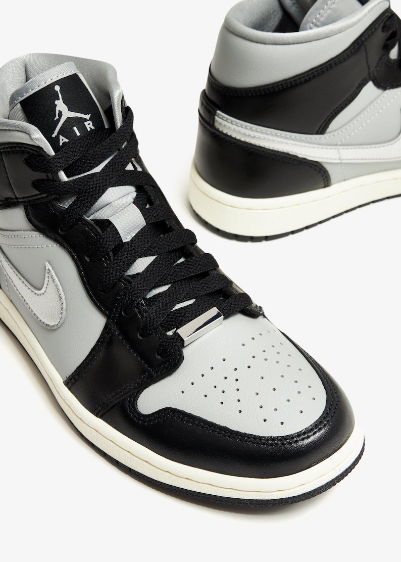 Op de afbeelding: Paar hoge sneakers in zwart, grijs en wit. De sneakers hebben zwarte veters, een grijze neus en een witte zool. Het Air Jordan-logo is zichtbaar op de tong. Geschikt voor sport en dagelijks gebruik.