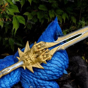 May include: A gold and silver sword with a detailed design. The sword has a golden handle with a dragon head and claws. The blade is silver with intricate engravings.
