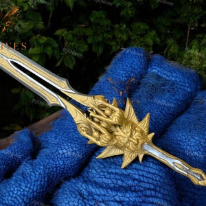 May include: A gold and silver sword with a detailed design. The sword has a handle with a sculpted design of a face with multiple hands.