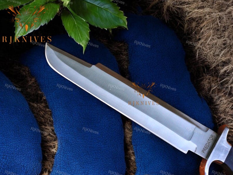 May include: A silver knife with a black handle and the word "PREDATOR" printed on the blade. The knife is lying on a blue surface.