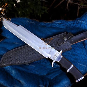 May include: A silver and black hunting knife with a leather sheath. The knife has a black handle with a silver metal guard and a silver blade with the word "PREDATOR" etched on it.