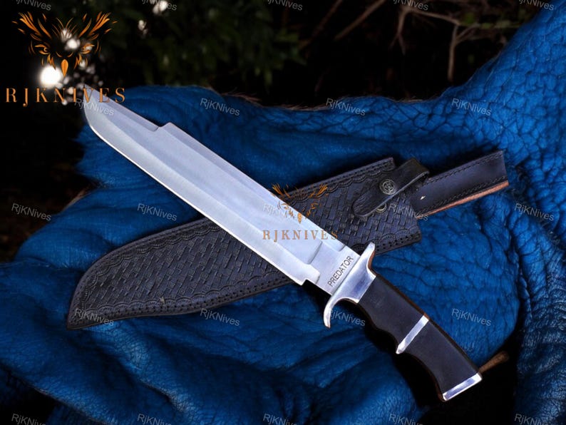 May include: A silver and black hunting knife with a leather sheath. The knife has a black handle with a silver metal guard and a silver blade with the word "PREDATOR" etched on it.