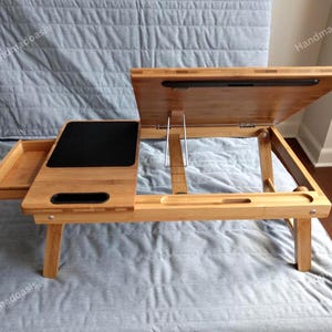 May include: A natural bamboo laptop desk with a black surface for a mouse and a tilting top. The desk has a pull-out drawer and adjustable legs. The desk is 28 inches long, 14 inches wide, and 10 inches high.