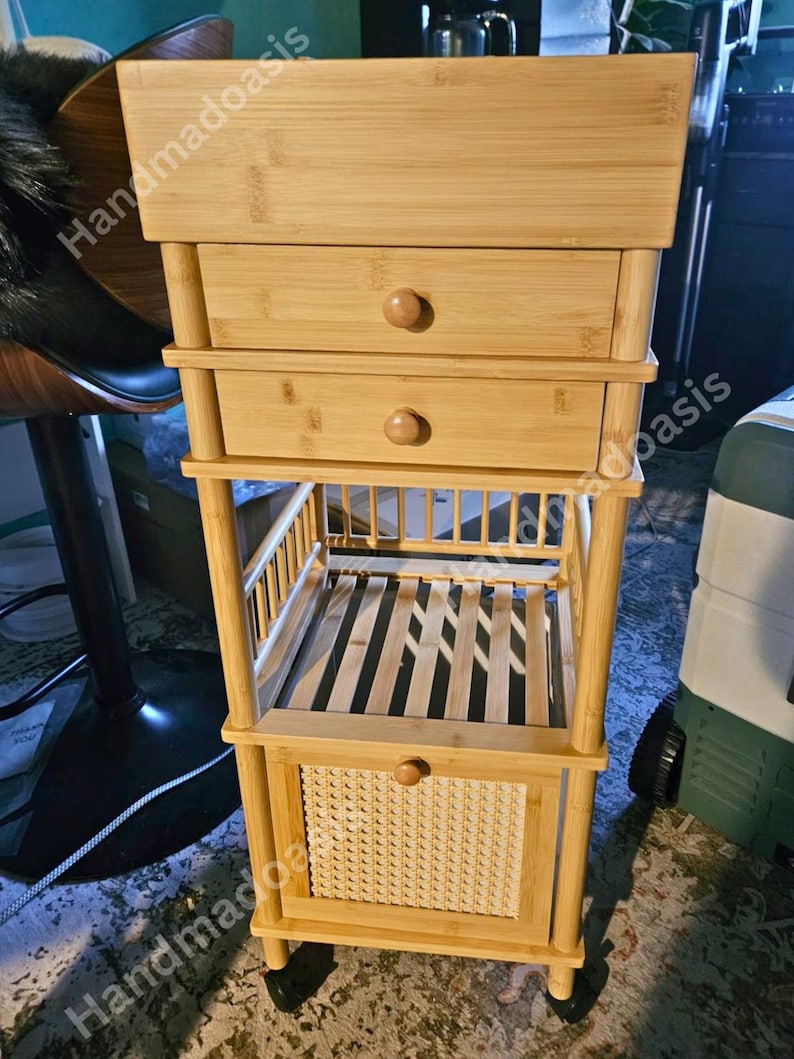 May include: A light-colored bamboo storage cart with two drawers, a slatted shelf, and a woven basket-style drawer. The cart has a rectangular top and is supported by four legs with small wheels.
