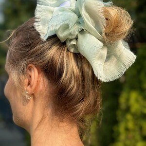 Può includere: Un elastico per capelli blu chiaro con un bordo sfrangiato. L'elastico è legato attorno a una coda di cavallo.