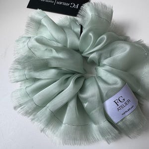 May include: A light green hair scrunchie with a frayed edge and a white label that says "FG Atelier" and "fgatelier.com".