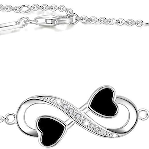 May include: A silver chain bracelet featuring a black enamel infinity symbol and small heart charms. The infinity symbol is embellished with clear cubic zirconia stones.