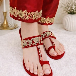 May include: Red sandals with gold floral embroidery and matching red pants with gold floral embroidery at the hem. The sandals have a T-strap design. The pants are made of a silky material.