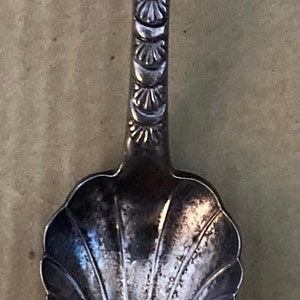 May include: Antique silver spoon with ornate floral and leaf design on the handle and bowl. The spoon's handle features a series of decorative elements. The spoon is likely used for serving or eating.