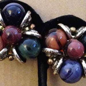 May include: Vintage clip-on earrings featuring clusters of colorful, round beads. The earrings showcase a mix of colors, including red, purple, green, and blue, with silver-tone metal accents. A unique and eye-catching accessory.