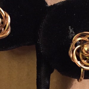 May include: A pair of gold-toned screw-back earrings featuring a central polished sphere surrounded by a series of interlocking circular wire loops that create a layered, dimensional flower-like design with a warm metallic finish.