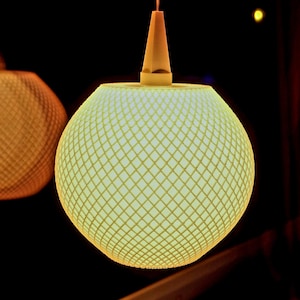 Könnte beinhalten: Eine weiße Pendelleuchte mit einem geometrischen, rautenförmigen Muster. Die Leuchte ist eingeschaltet und strahlt ein warmes, gelbes Licht aus.