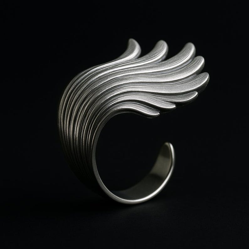 May include: A silver ring with a unique design that resembles a stylized wave or feather. The ring is made of smooth, polished metal and has a delicate, flowing shape.
