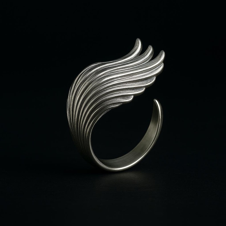 May include: A silver ring with a wing design. The wing is made of many thin, curved lines that create a flowing, organic shape.