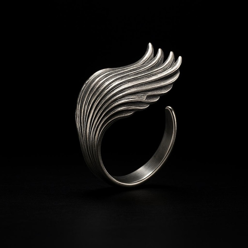 May include: A silver ring with a wing design. The wing is made of many thin, overlapping layers, creating a textured and intricate look.