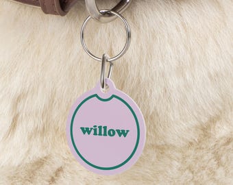 Puede incluir: Una chapa redonda para perro de color lila claro con un borde verde y la palabra "willow" escrita en letras verdes.