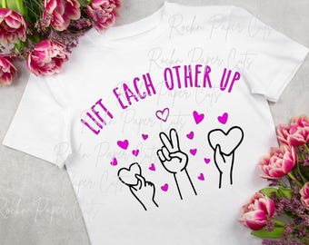 Könnte beinhalten: Weißes T-Shirt mit dem Text "Lift Each Other Up" in lilafarbener Schrift. Das Design enthält rosa Herzen und schwarze Handgesten.