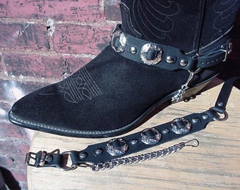 May include: Black leather cowboy boots with a silver buckle and a chain attached to a leather strap. The strap has silver conchos.