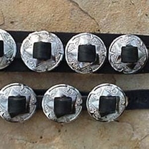 Puede incluir: Dos pulseras de cuero negro con cascabeles plateados. Cada pulsera tiene cinco cascabeles con un dise&ntilde;o en relieve.